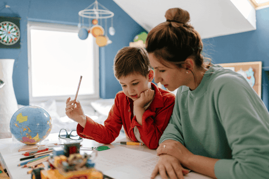 Mother helping her young son with schoolwork at a desk covered in pencils, a globe, and learning materials.