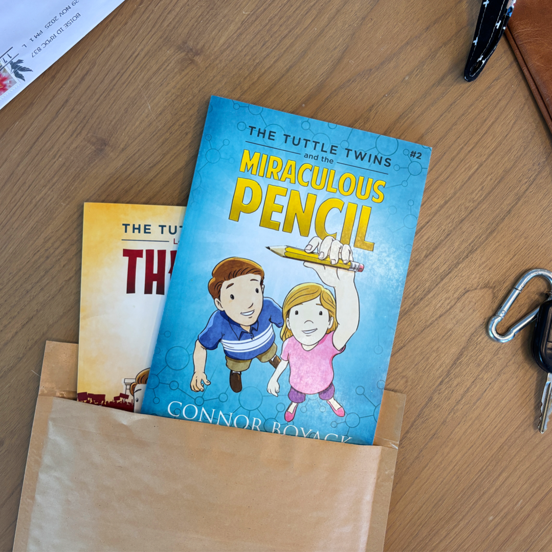 Book titled 'The Tuttle Twins and the Miraculous Pencil' on a wooden surface with a paper bag and keys.