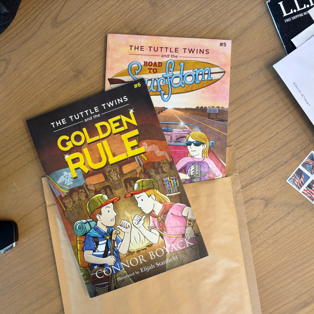 Two books titled 'The Tuttle Twins and the Golden Rule' and 'The Tuttle Twins and the Road to Surfdom' on a wooden surface.