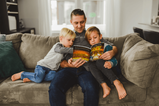 A father sits on a couch with his two young sons while reading "The Golden Rule" together.