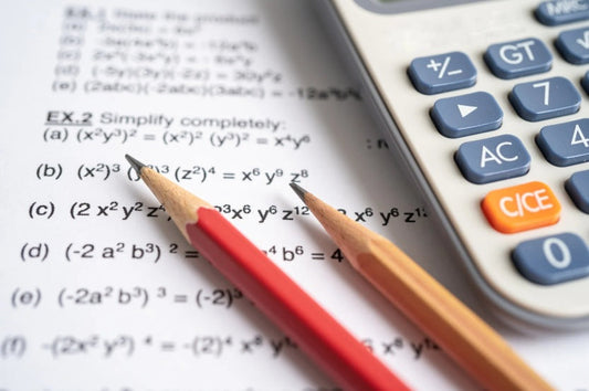 A printed algebra worksheet, with a red pencil and a sharpened wooden pencil resting across the page beside a grey scientific calculator. Image by sasirin pamai on Canva