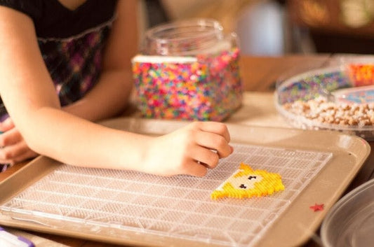 A child arranging small colorful beads on a pegboard to make a pixel-style craft design.
