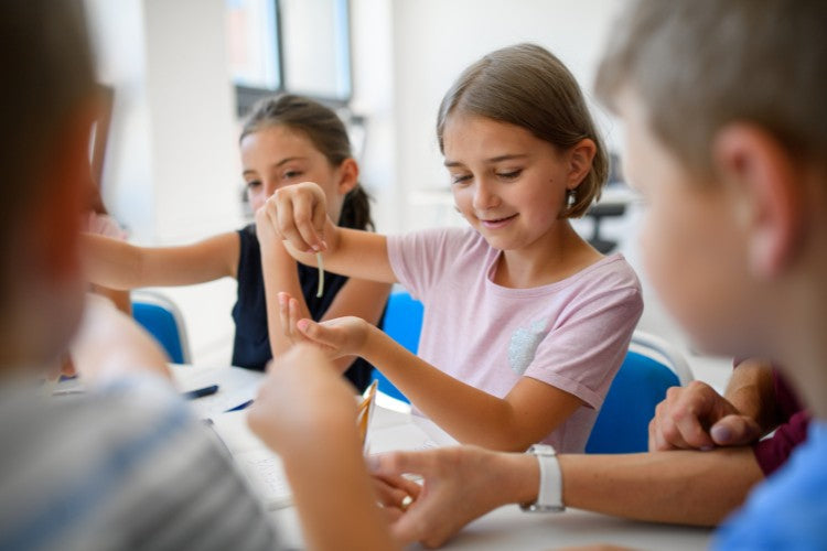 A group of children sit around a table examining an object during a collaborative classroom activity.