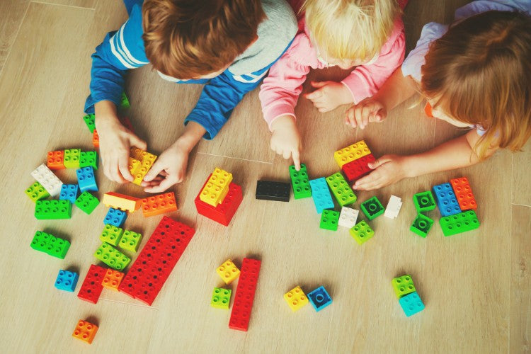 A group of children sit on the floor and play with bright, colorful building blocks together. [Photo by Nadezhda1906 from Canva]