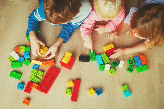 A group of children sit on the floor and play with bright, colorful building blocks together. [Photo by Nadezhda1906 from Canva]