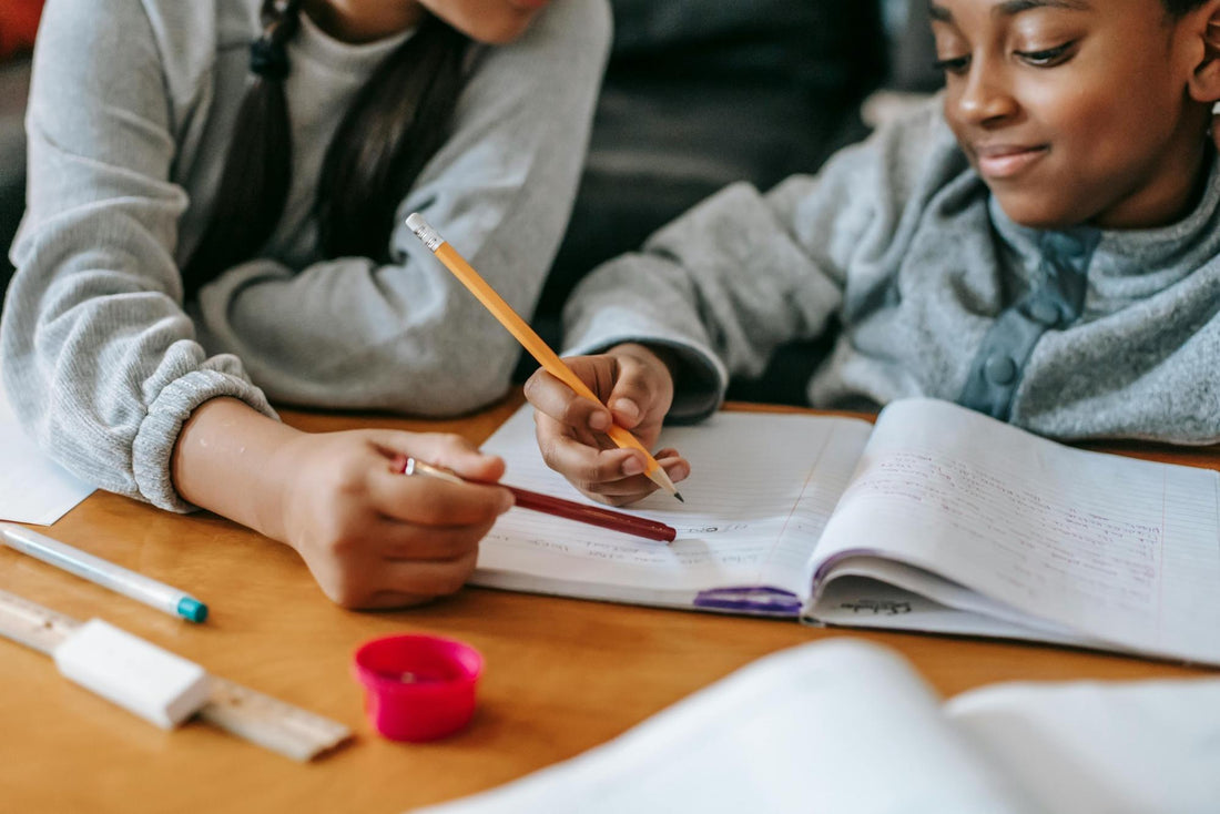 Children sitting together at a table working on school assignments with pencils and notebooks.