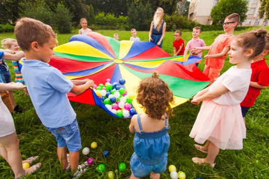 Group of children holding a large colorful parachute filled with plastic balls during outdoor playtime.