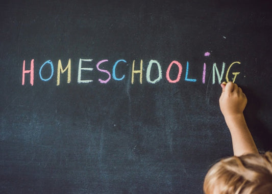 Child writing "HOMESCHOOLING" in colorful chalk on a blackboard.