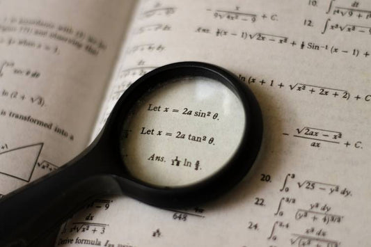 A magnifying glass placed on top of an open math book, enlarging algebraic equations and formulas.