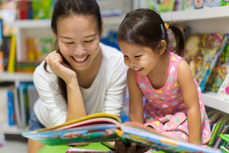 A joyful mother and young daughter reading a colorful book together in a library or bookstore setting, promoting child literacy.