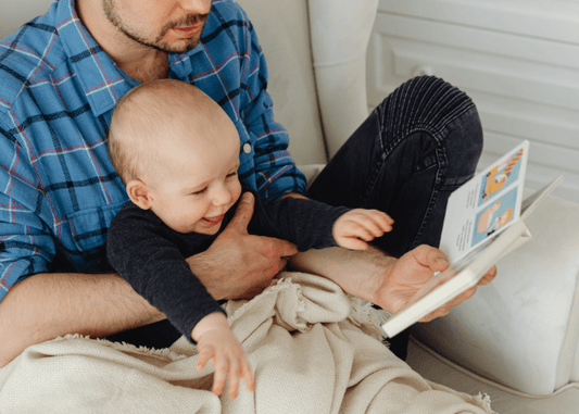 Baby sitting on a parent’s lap and reaching for a picture book during storytime.