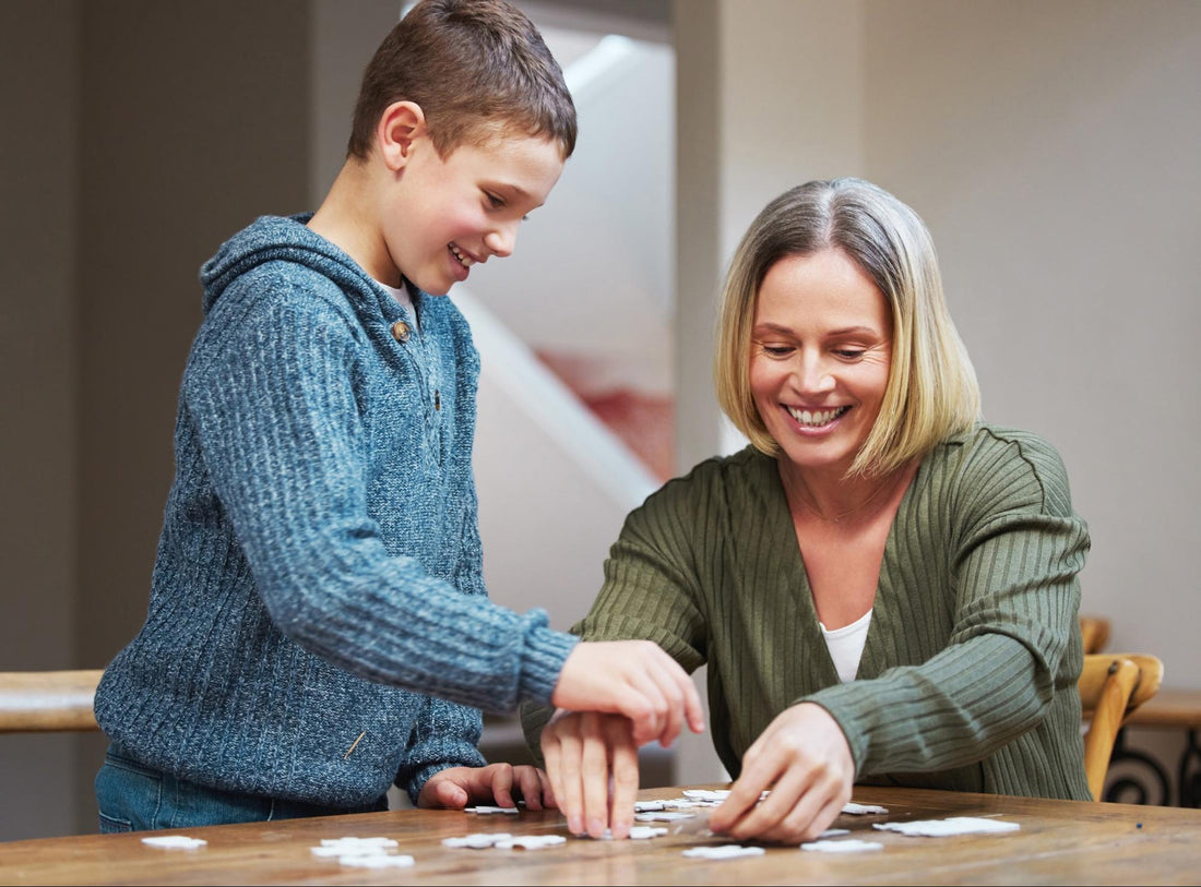 A smiling parent and child working together to assemble a jigsaw puzzle at a table.