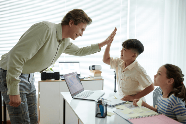 A teacher giving a high five to a student while others watch during a classroom activity.