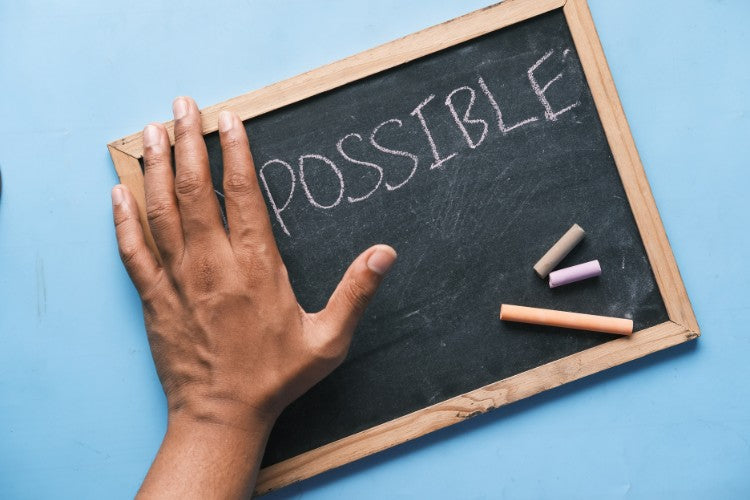 A hand rests on a small chalkboard with the word “possible” written in chalk against a blue background.