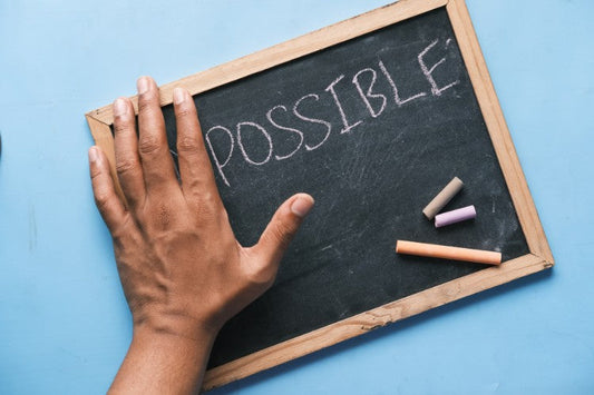 A hand rests on a small chalkboard with the word “possible” written in chalk against a blue background.
