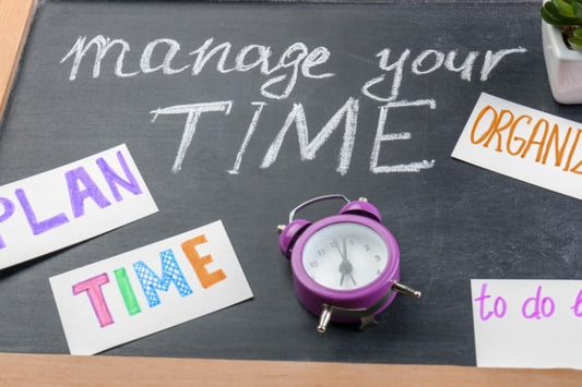 Chalkboard with the words “manage your time” written on it, surrounded by colorful labels and a small purple alarm clock.