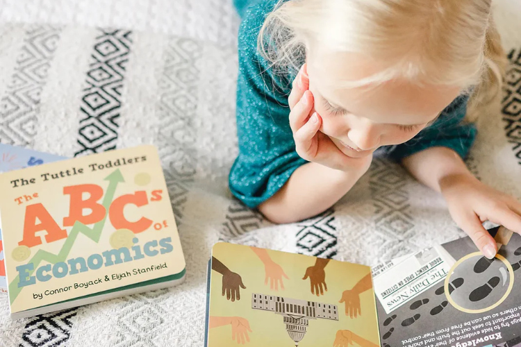 Toddler reading The Tuttle Toddlers ABCs of Economics children’s book.