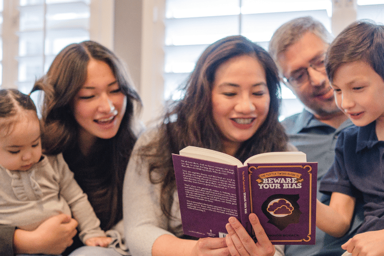 A family of five sitting together and smiling while reading "The Tuttle Twins Guide to Beware Your Bias.