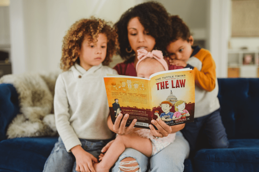 A mother sitting on a blue couch reading The Tuttle Twins Learn About The Law aloud to her three children.