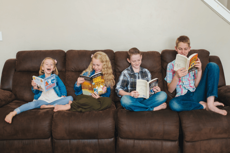 Four children of different ages sitting on a brown couch reading various Tuttle Twins books.