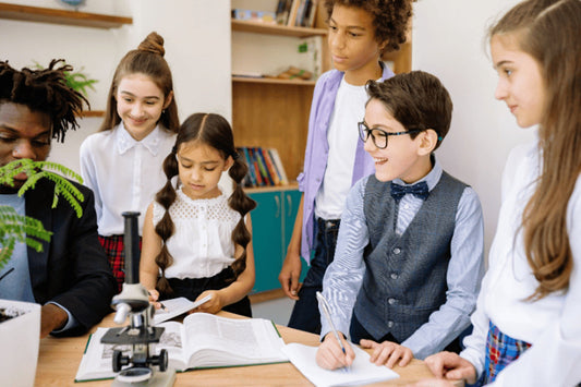A group of diverse students and their teacher gather around a microscope and a textbook to study a plant.