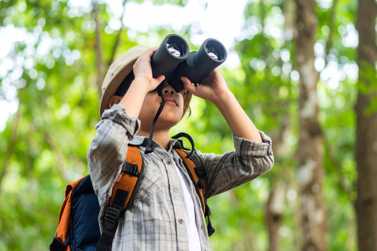 Child using binoculars while exploring nature outdoors.