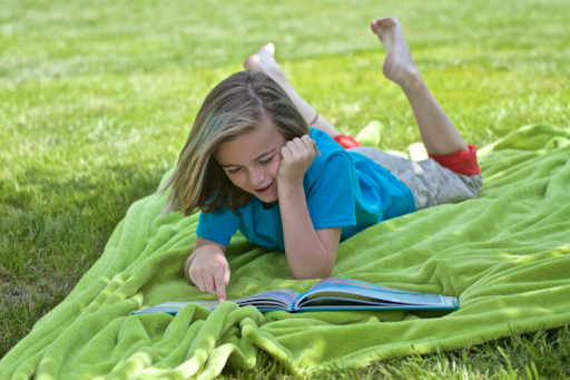 Child reading a book outdoors on a blanket.