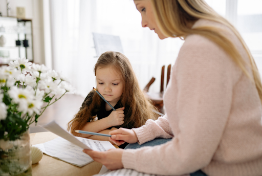 Mother helping child with homeschooling lessons at home.