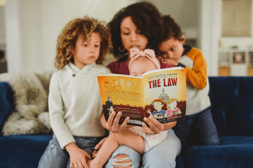 A mother sits on a blue velvet sofa reading The Tuttle Twins Learn About The Law to her three children.