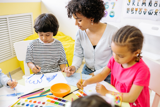 Teacher helping children draw and paint at table.